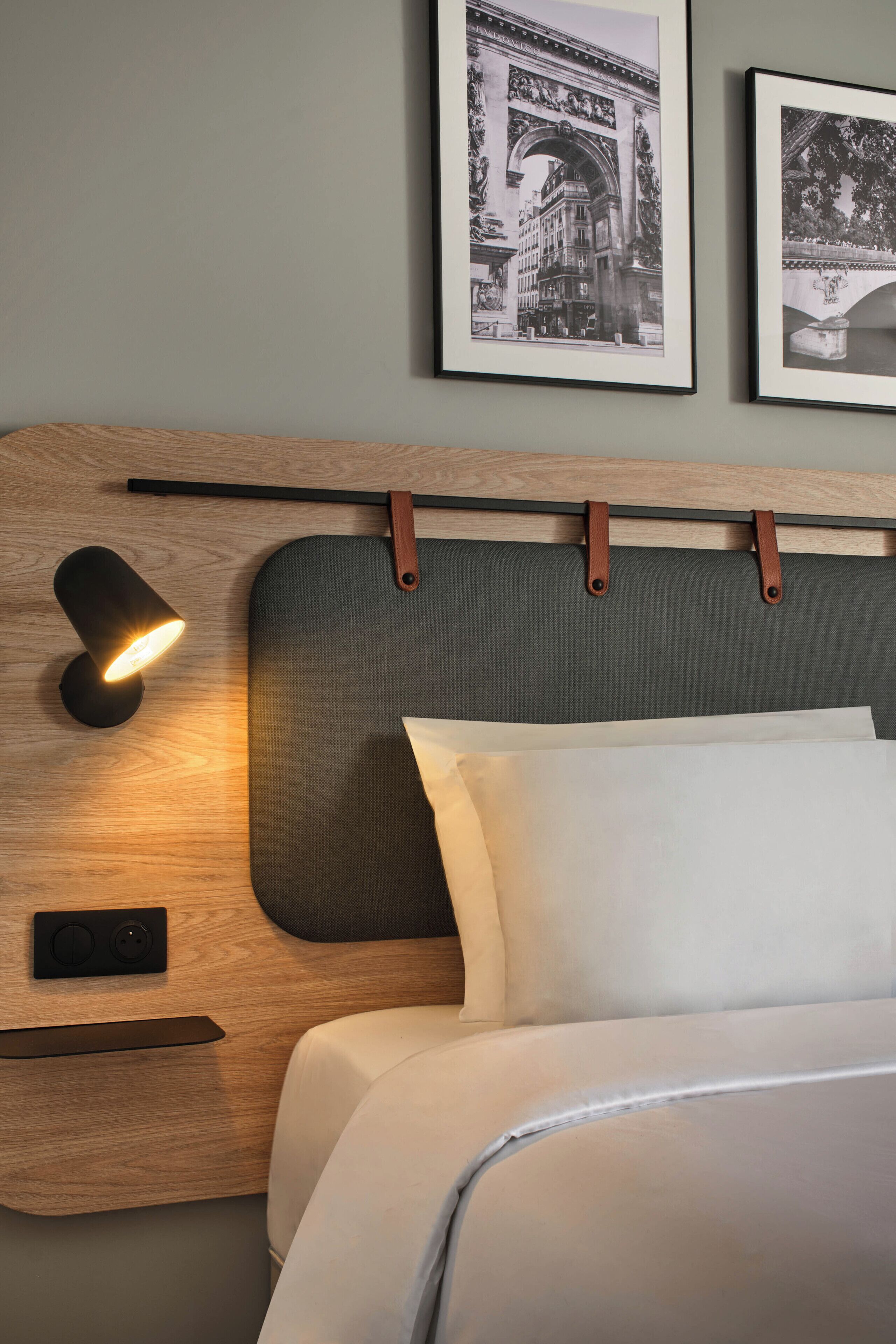 Una cama bien hecha con cabecera, una lámpara de noche y dos cuadros en la pared.