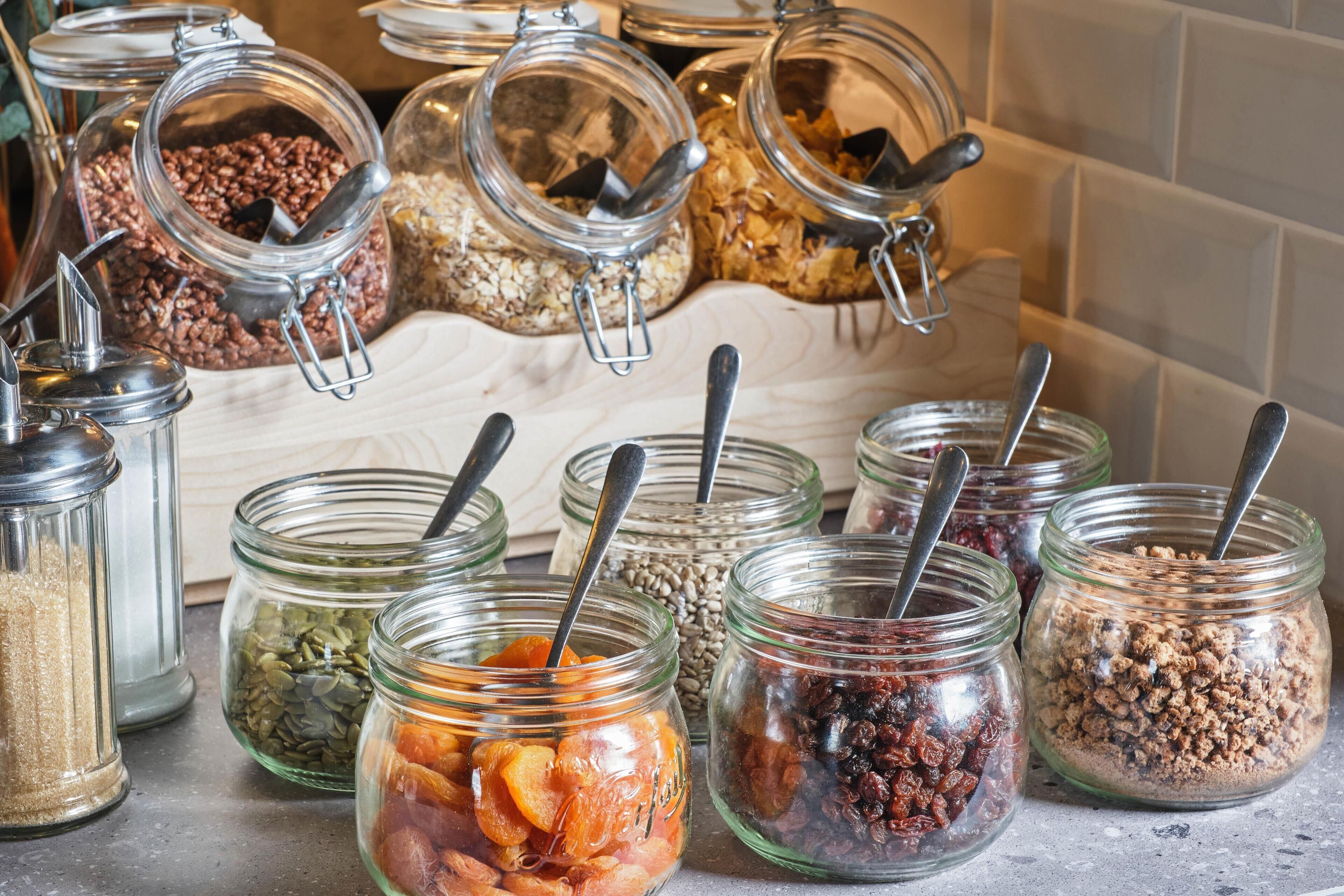 Multiple glass jars with metal lids and spoons, containing various dried fruits and nuts.