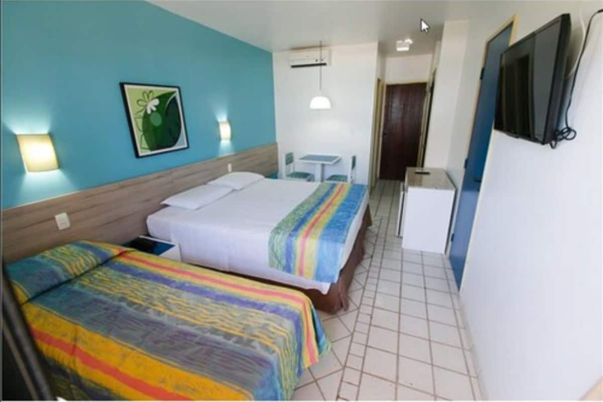 Habitación de hotel con dos camas, un escritorio, una silla, un refrigerador pequeño y un televisor montado en la pared.