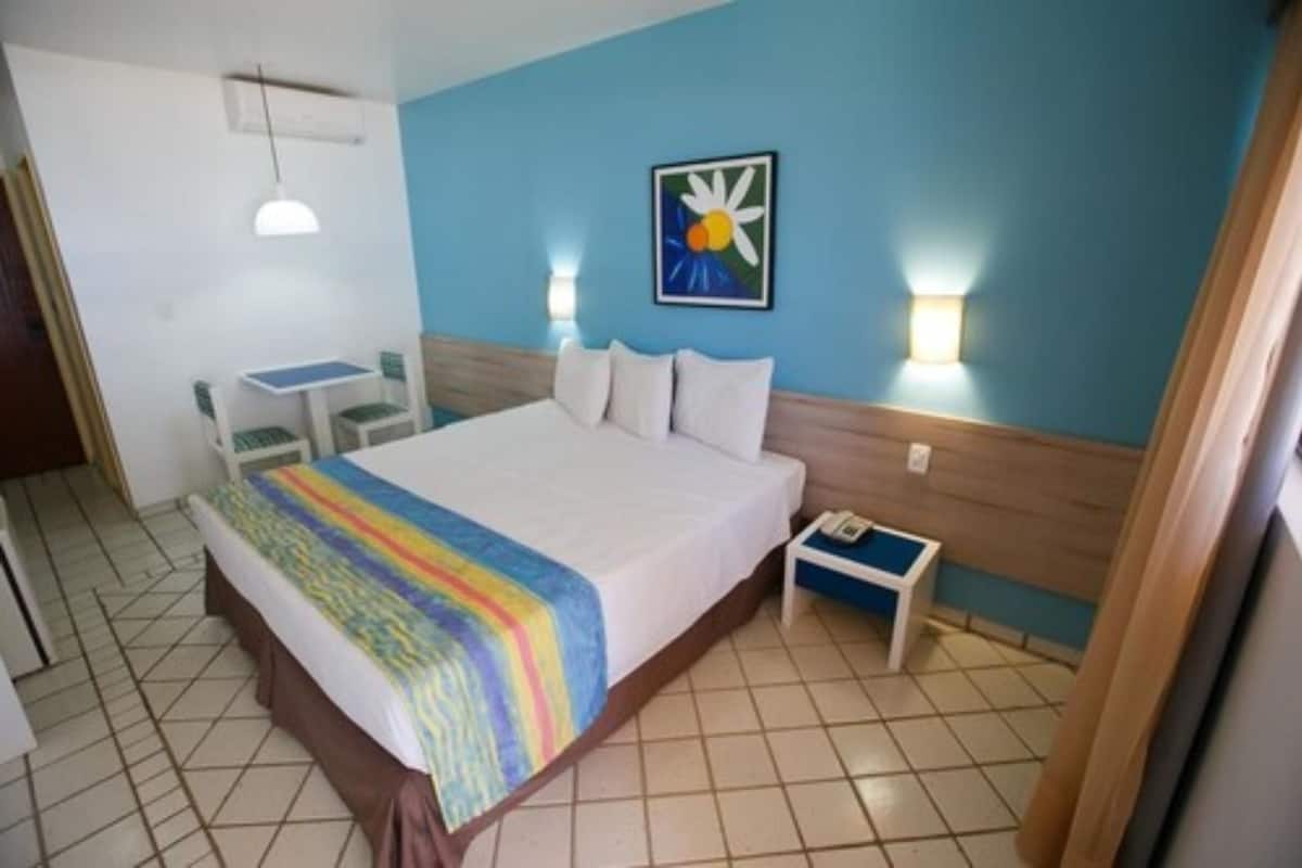 Habitación de hotel con cama, mesita de noche, una silla, una pequeña mesa y una obra de arte en la pared.