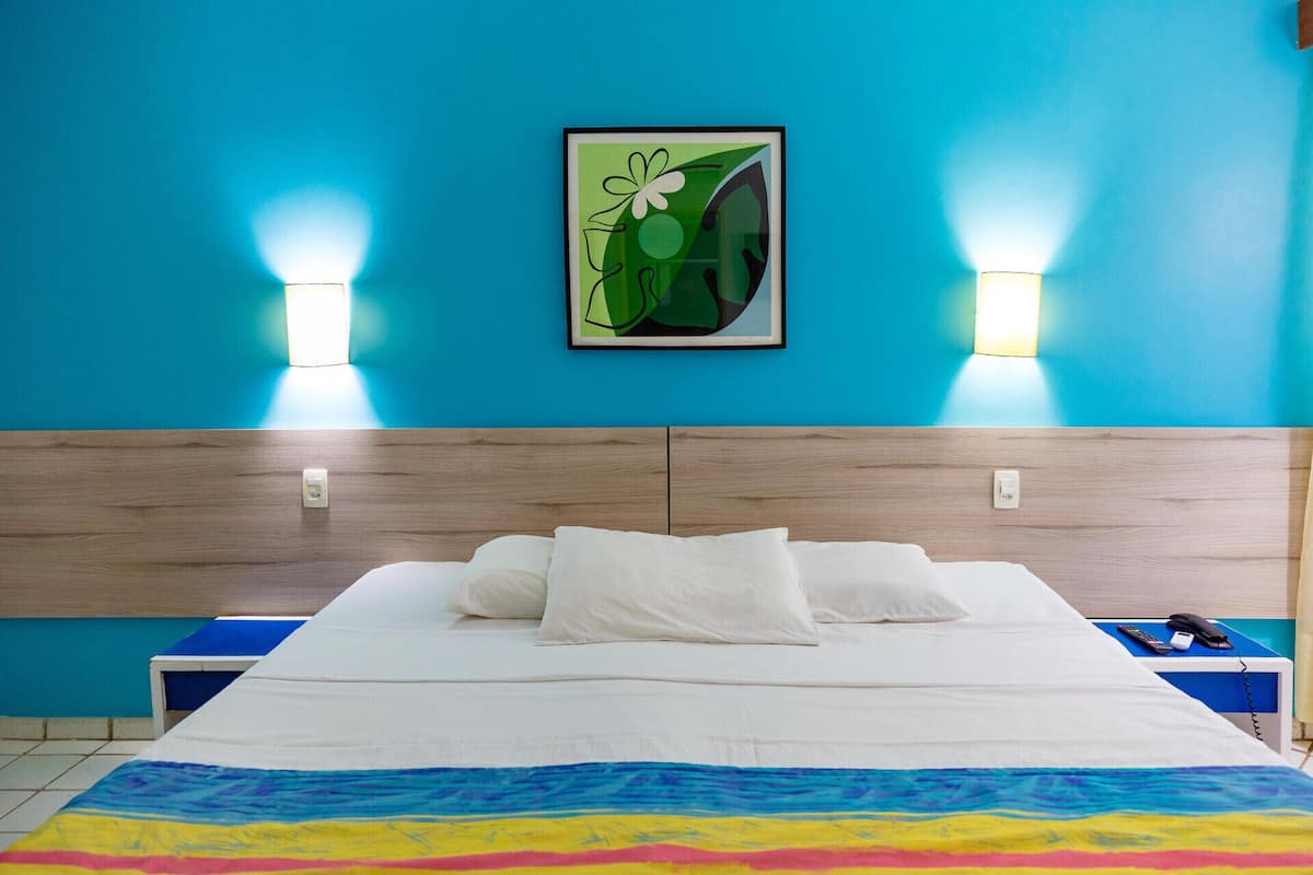Habitación de hotel con cama, dos mesitas de noche, lámpara y un cuadro en la pared.