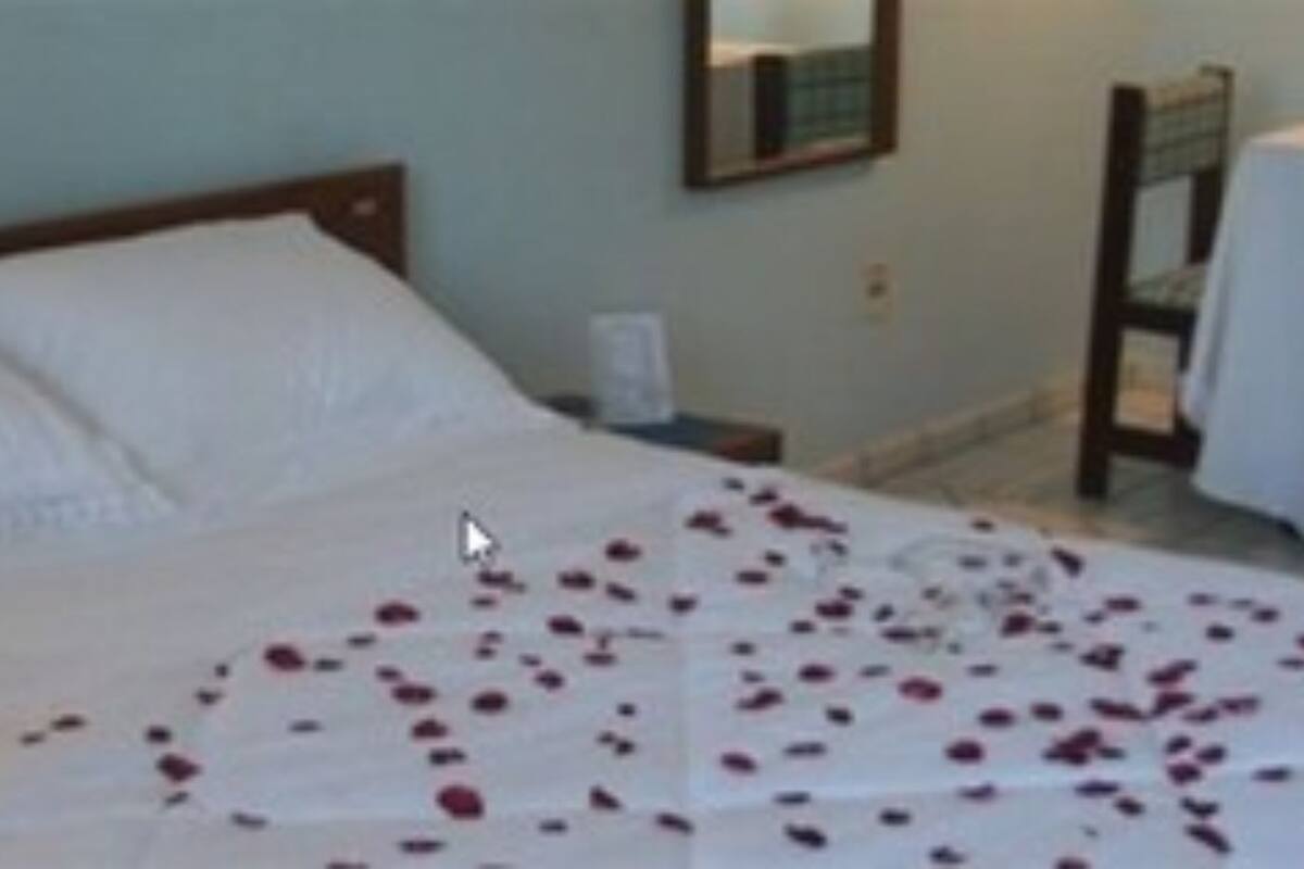 Una cama bien hecha con sábanas blancas, una mesita de noche con una lámpara y una pequeña mesa con una botella y un vaso.
