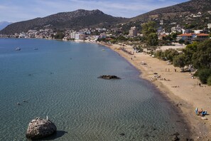 A coastal town with a clear beach, rocky outcrops, and buildings in the background. - Hotel Tolo (Nafplio)