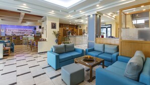 A hotel lobby with blue sofas, a coffee table, a reception desk, and a bar area. - Hotel Tolo (Nafplio)