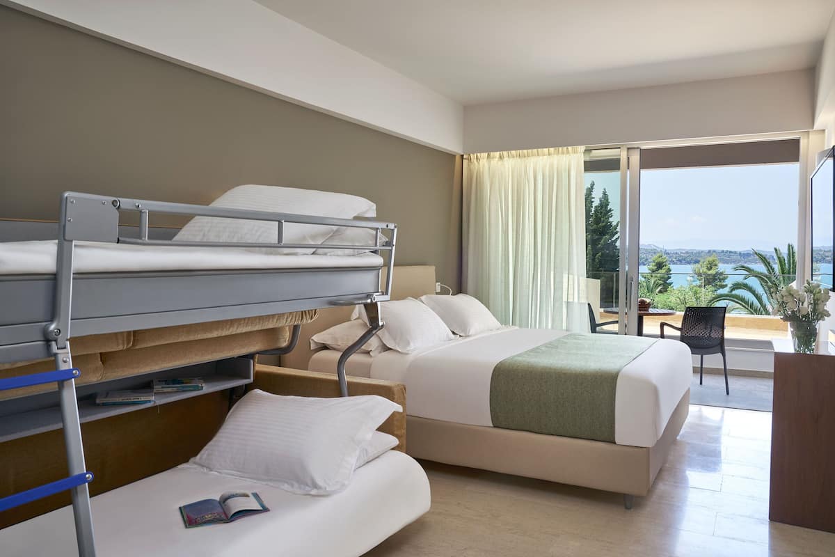 A hotel room with a bunk bed, a single bed, and a balcony with a view of the sea.