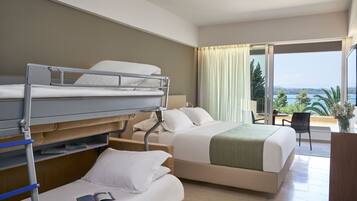Une chambre d’hôtel avec un lit superposé, un lit simple et un balcon donnant sur la mer.