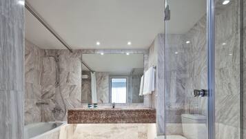 Une salle de bain moderne dotée d’une douche à parois de verre, d’un espace de douche carrelé en marbre, d’une baignoire et de toilettes.