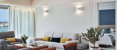 A modern hotel room with a sofa, a dining table, and a potted plant.