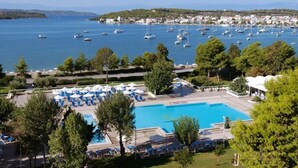 Un resort con una piscina grande, sillas de descanso y vistas al mar con barcos.