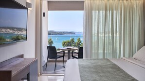 Habitación de hotel con cama, televisor montado en la pared, balcón con mesa y sillas y vista al mar.