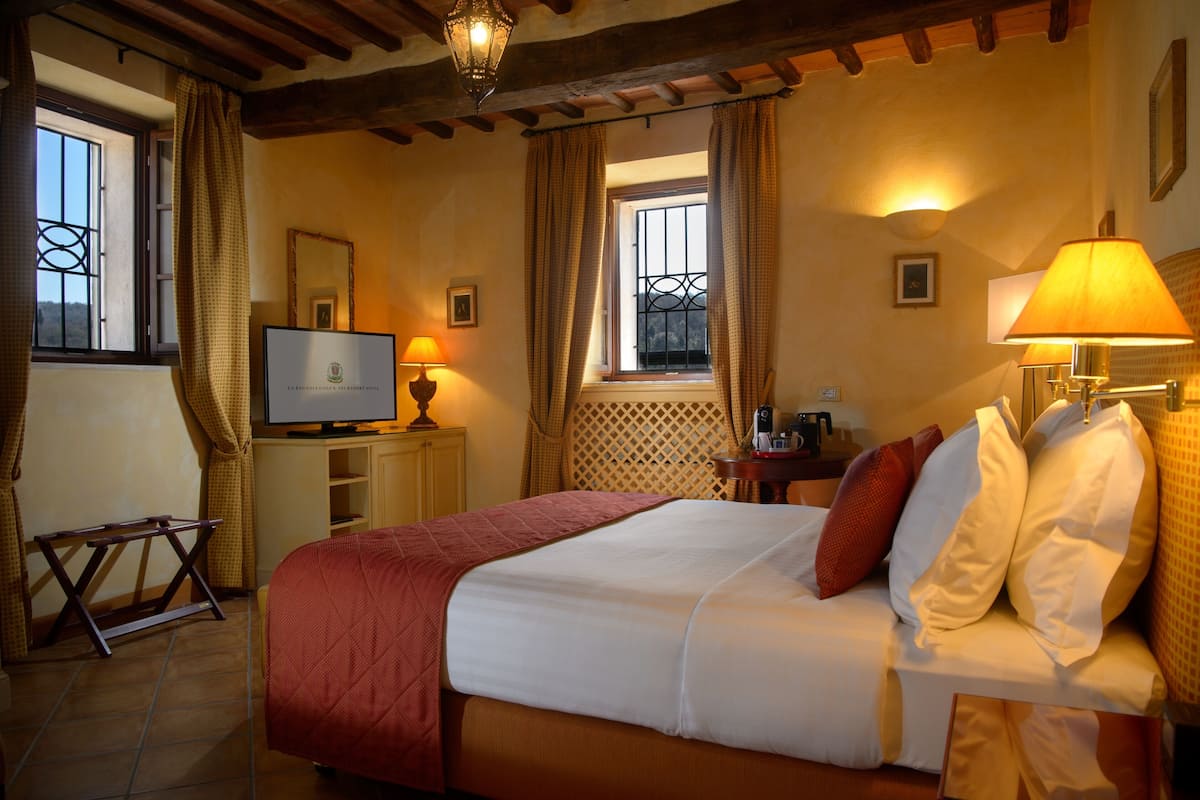 A hotel room with a bed, a television, a table with a lamp, and a window with curtains.