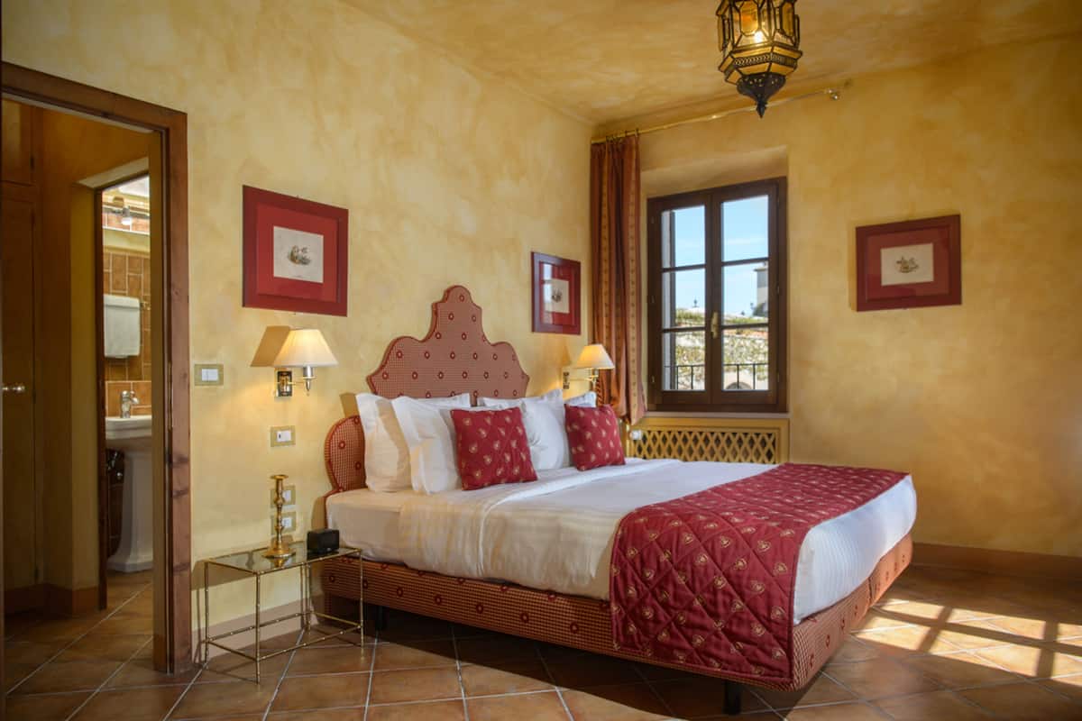 A hotel room with a large bed, two bedside tables, a window with curtains, and framed pictures on the walls.