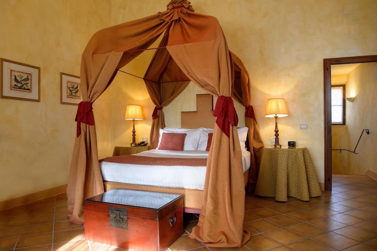A four-poster canopy bed with a nightstand and lamp, a bedside table, and a chest of drawers.