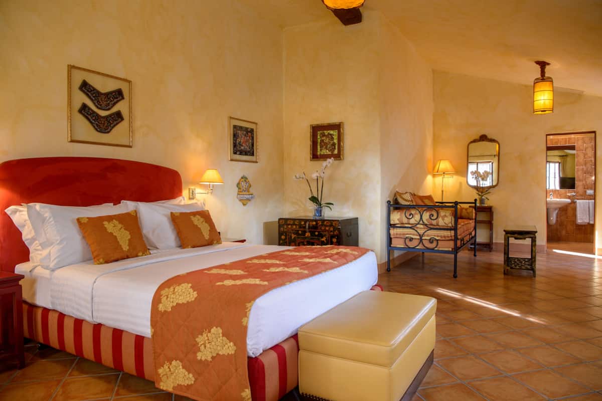 A hotel room with a large bed, a small table, and a mirror.