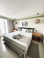 Un cuarto de hotel ordenado con una cama grande, una mesita de noche, una lámpara de pared y un cuadro enmarcado en la pared.