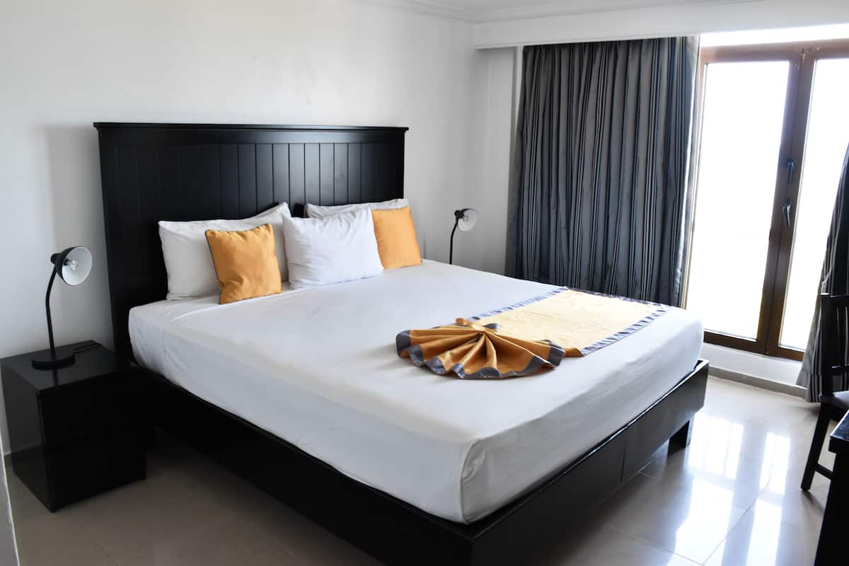 Une chambre d’hôtel avec un grand lit, une table de chevet, une lampe et une vue sur l’extérieur par une fenêtre munie de rideaux.