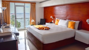 Ein Hotelzimmer mit einem großen Bett, einem Schreibtisch mit Lampe, einem Sessel und Blick auf das Meer durch das Fenster.