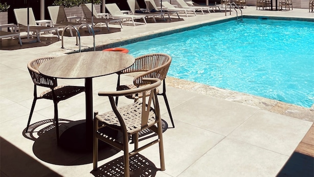 Ein Hotelpoolbereich mit Liegestühlen und Sonnenschirmen, ein Schwimmbecken und im Hintergrund ein Gebäude mit Balkonen.