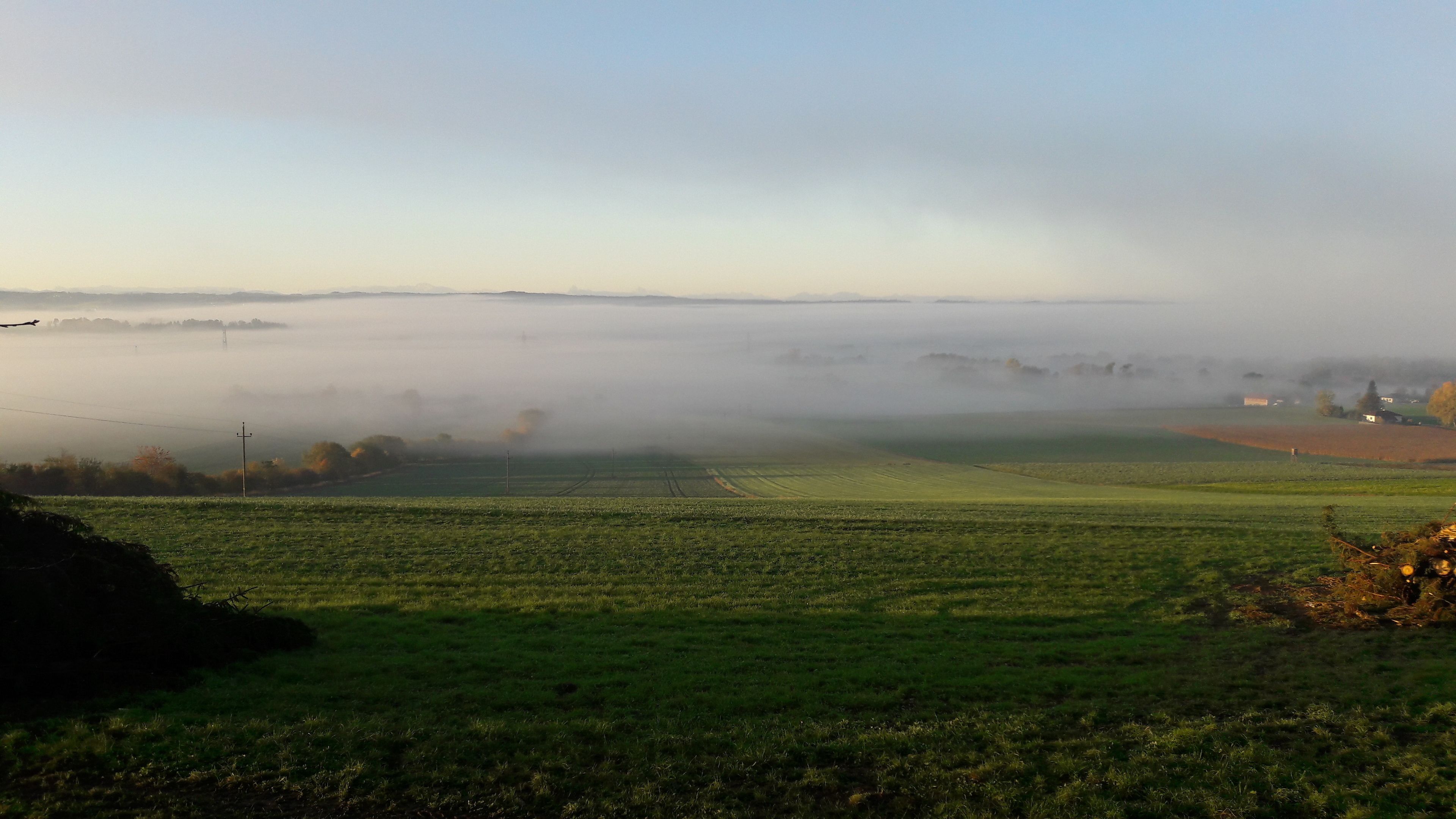 Eine neblige Landschaft mit Feldern und Gebäuden in der Ferne.