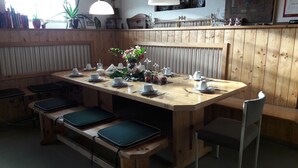 A wooden dining table set with white cups, saucers, and plates, surrounded by benches with green cushions. - Geinberg Suites & Vianova Lodges (Polling im Innkreis)