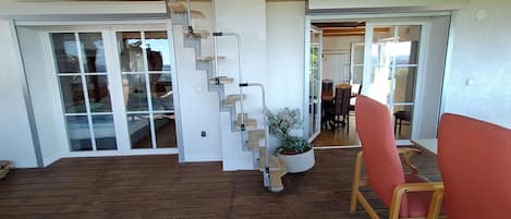 A wooden deck with a staircase leading to a glass door, a potted plant, and a dining area with chairs.