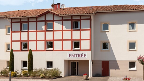 A building with a sign reading "ENTRÉE" at the entrance, featuring a traditional facade with a tiled roof and multiple windows.