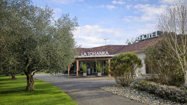 Una entrada de hotel con un área de estar techada al aire libre, un camino pavimentado y un césped bien cuidado.
