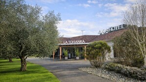 A hotel entrance with a covered outdoor seating area, a paved driveway, and a well-maintained lawn.