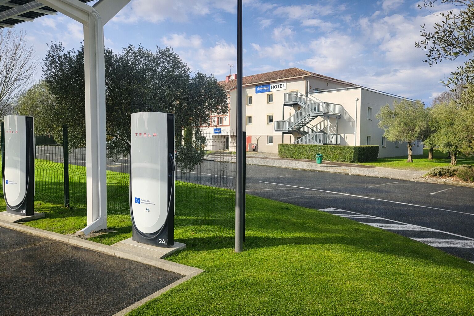 A hotel with a modern design, a staircase leading to the entrance, and a Tesla charging station nearby.