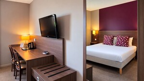 Habitación de hotel con escritorio, silla, televisión y cama con almohadas estampadas.