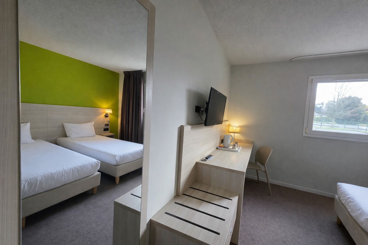 Habitació d'hotel amb dos llits, un escriptori amb cadira, televisió i finestra.