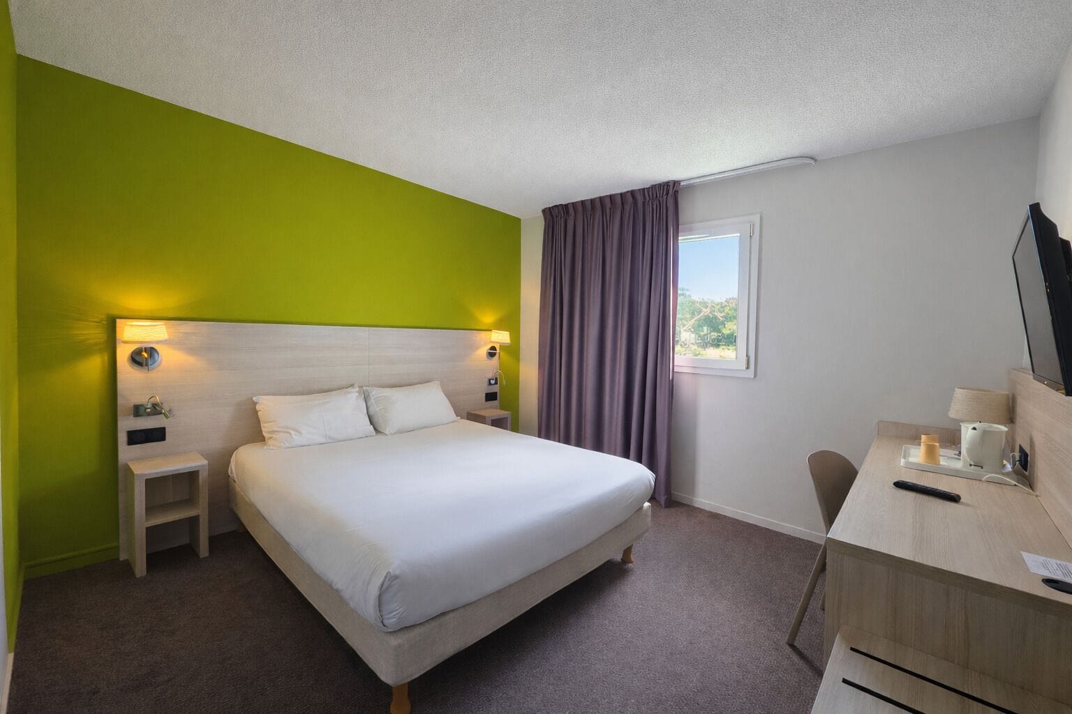 Una camera d'albergo con un letto, comodini, una scrivania, una sedia e una finestra con tende.