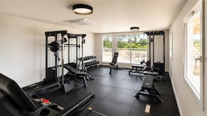 Un gimnasio con equipamiento para levantamiento de pesas, bancos y mancuernas.