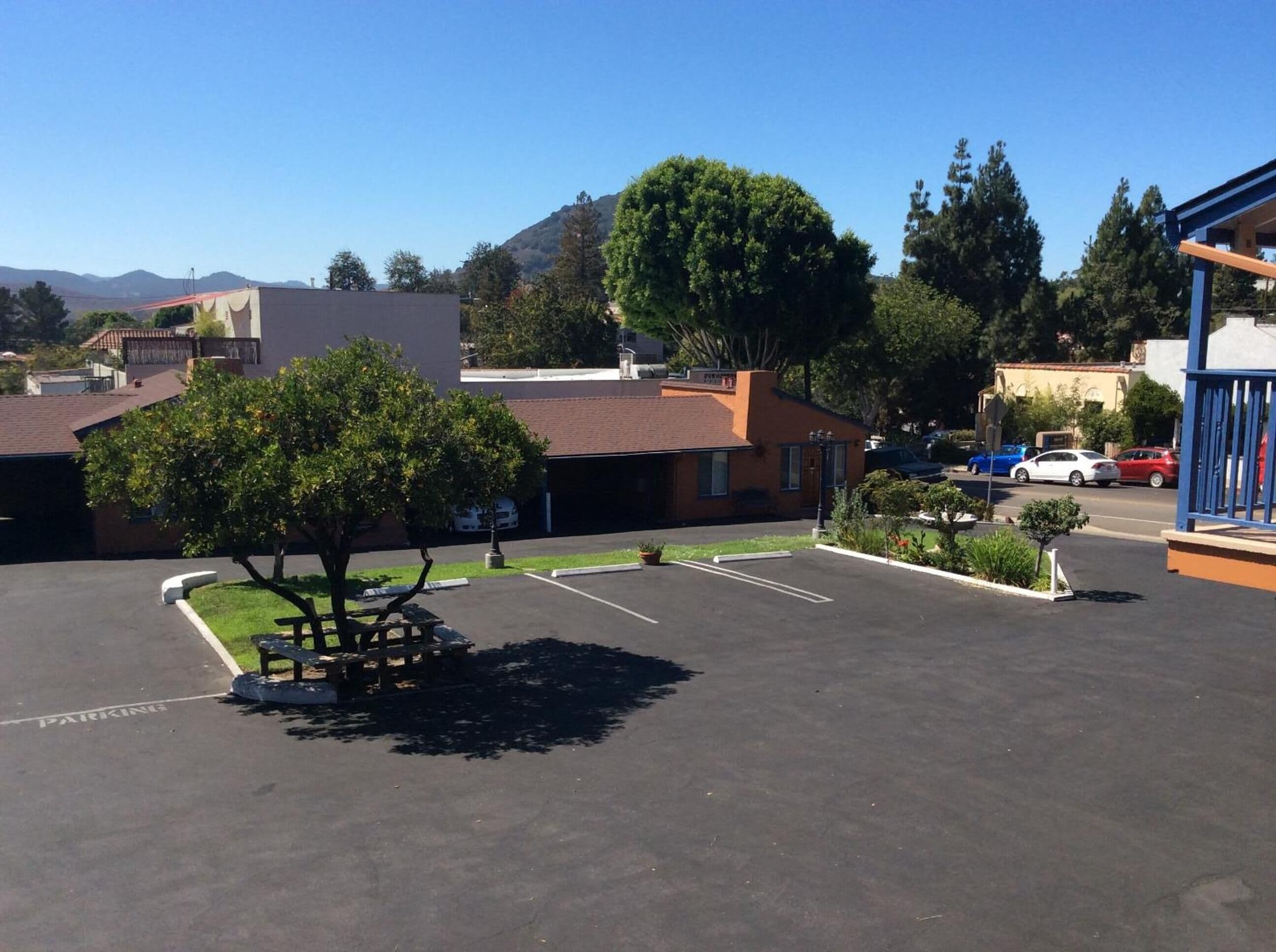 A parking lot with a picnic table and a tree, surrounded by buildings and a mountain in the background.