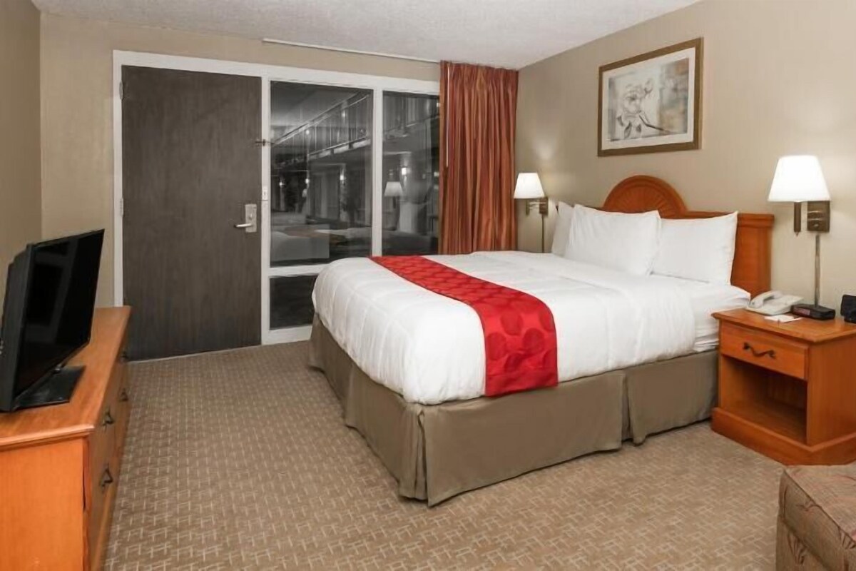 A hotel room with a bed, a TV, a desk, a chair, a nightstand, and a door leading to a balcony.