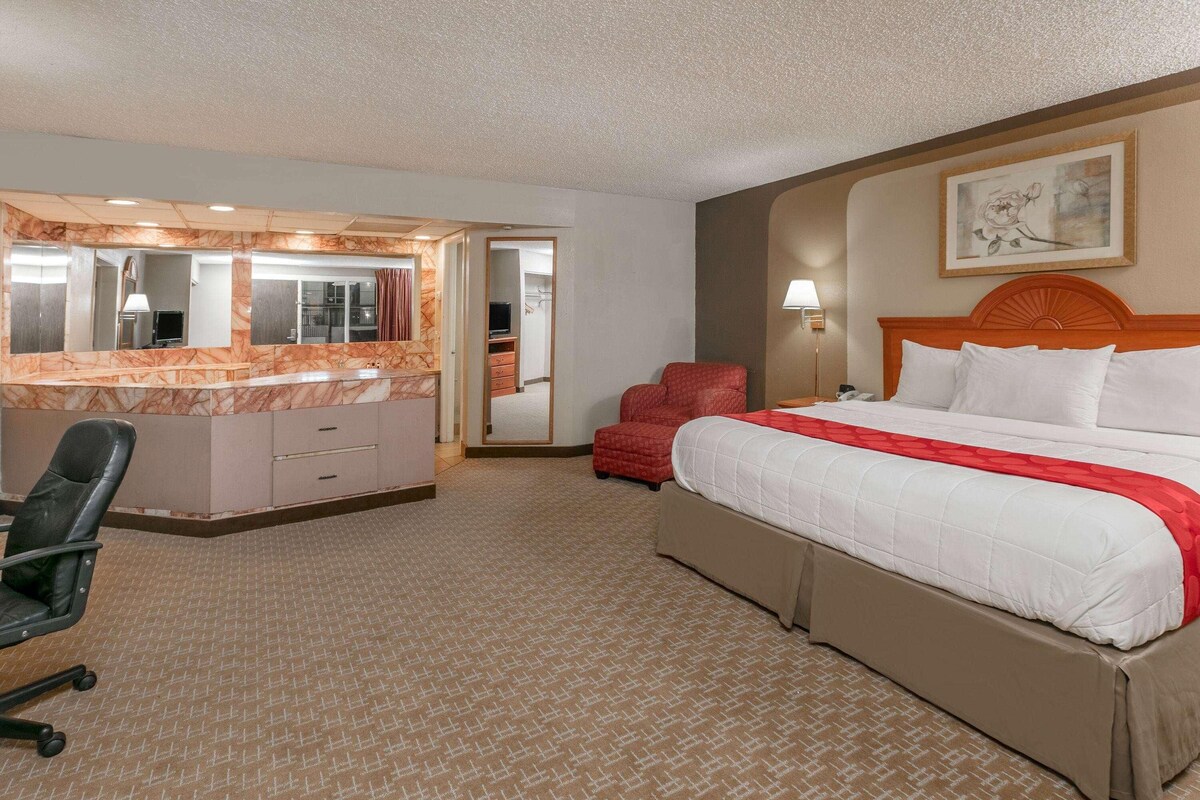 A hotel room with a bed, a desk with a chair, a mirror, and a door leading to a bathroom.