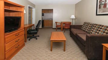A furnished living room with a television, sofa, coffee table, and a kitchen area in the background.
