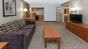 Un espacio habitable compacto con sofá, una mesita de madera, televisor, kitchenette y una puerta que da a un baño.