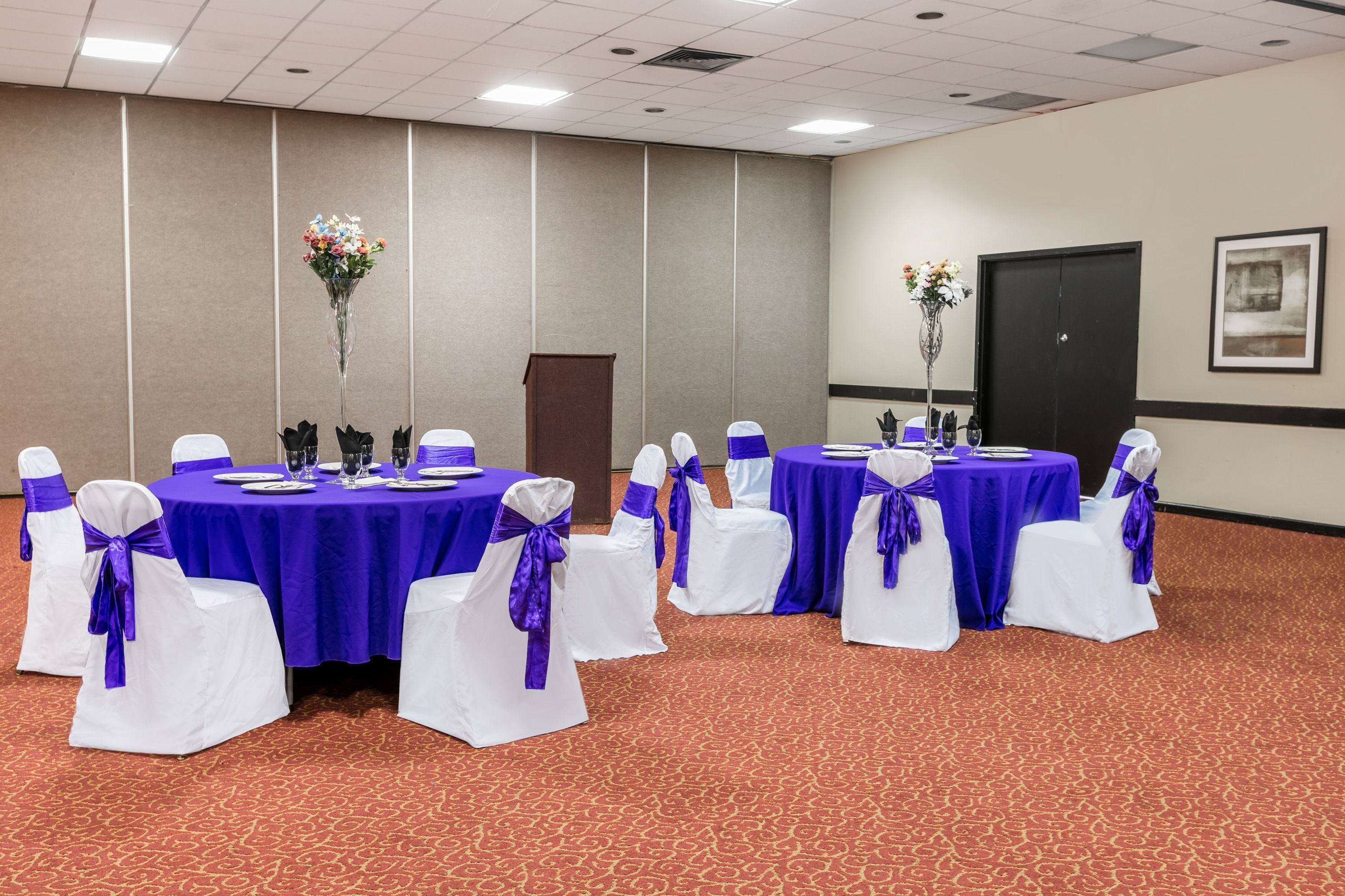 A conference room with tables set for a meeting, white chairs with purple sashes, and floral centerpieces.