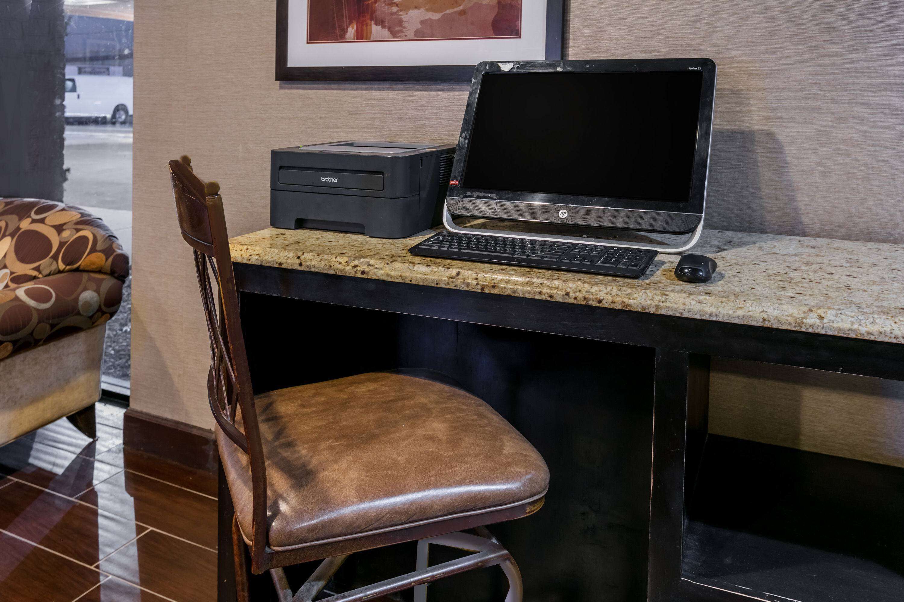 A laptop on a counter with a printer beside it, a chair, and a framed picture on the wall.