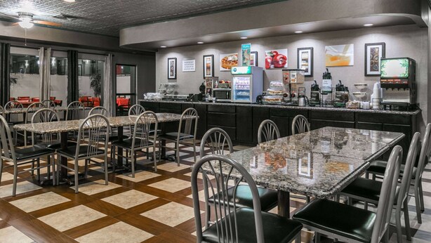Un restaurante con piso a cuadros, sillas y mesas de metal. Hay dispensadores de comida y bebida, y una barra con una máquina de café.