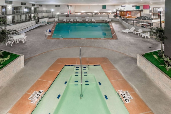An indoor swimming pool with a diving board, lounge chairs, and a poolside area with a railing.