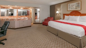 Una habitación de hotel con cama, escritorio con silla, espejo grande y sillón rojo.