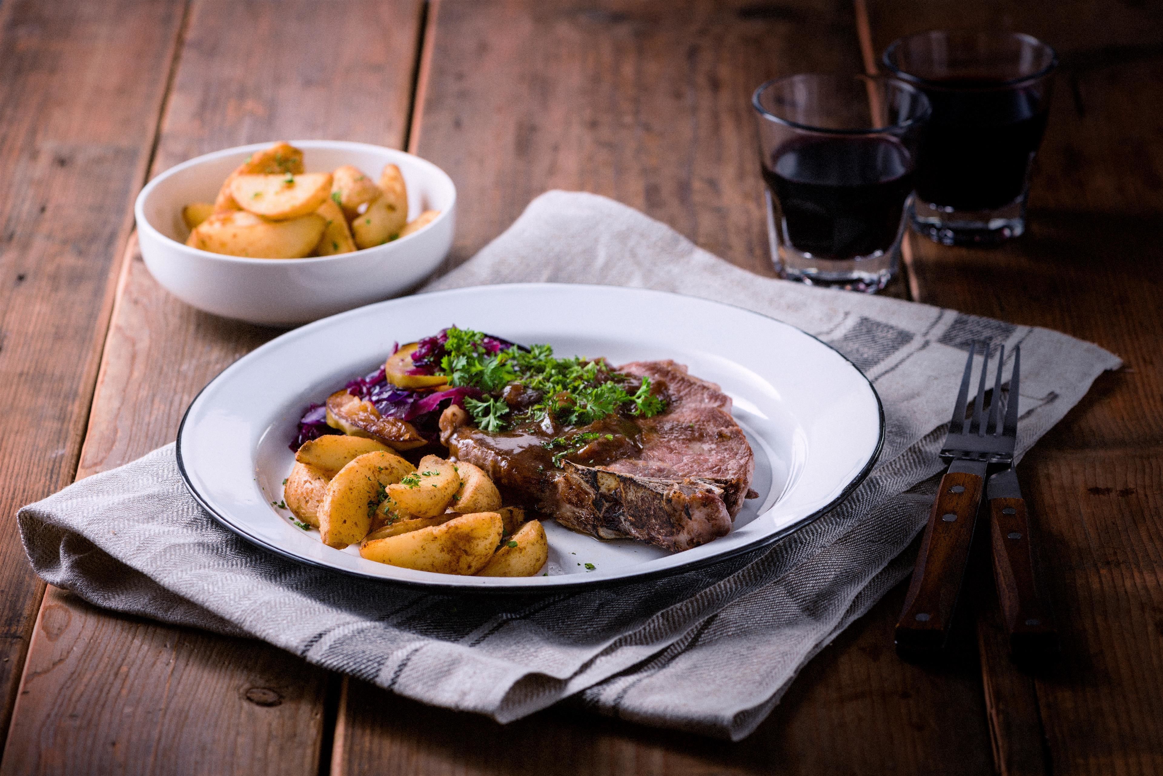 A plate of steak with potatoes and a side salad on a wooden table.