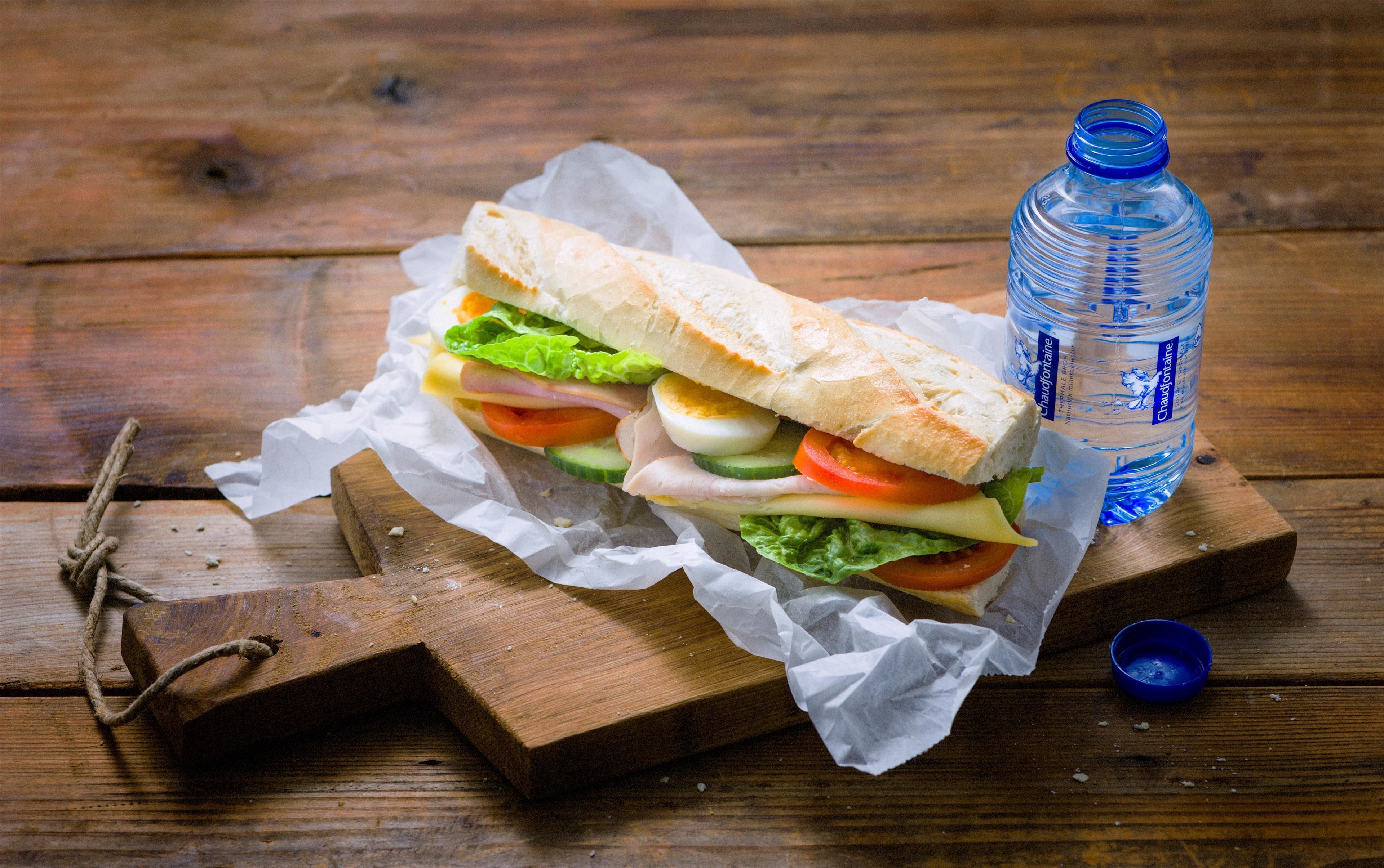 A sandwich on a wooden board with a water bottle beside it.