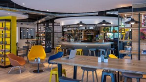 Eine moderne Bar mit gebogener Theke, Barhocker und verschiedenen Sitzgelegenheiten, darunter runde Tische und Stühle.