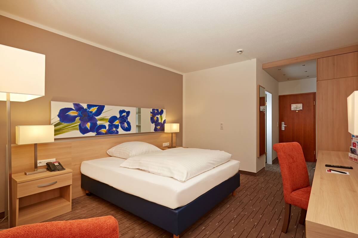 A hotel room with a bed, bedside table, lamp, and a chair.