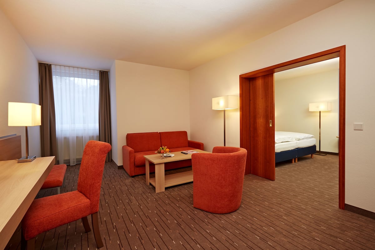 Une chambre d’hôtel avec un plancher en bois, un canapé, une table basse, un bureau avec une lampe et un lit.