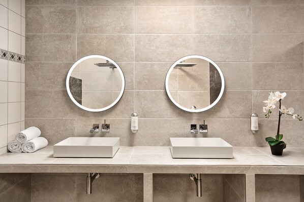 A modern bathroom with two sinks, each with a round mirror and a handheld showerhead. There are towels and a potted orchid on the counter. - Sunday Hotel Wiesbaden Niedernhausen (Niedernhausen)