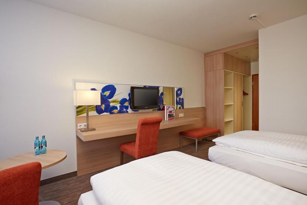 Hotellihuone, jossa on sänky, työpöytä tuolilla, televisio ja vaatekaappi.